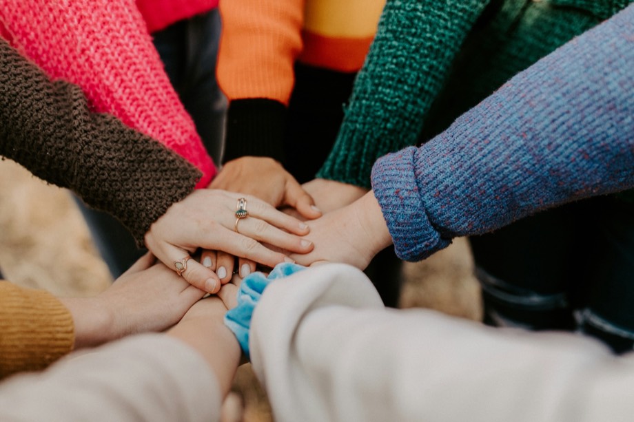 A diverse group of people stacking their hands together in a circle, representing collaborative support